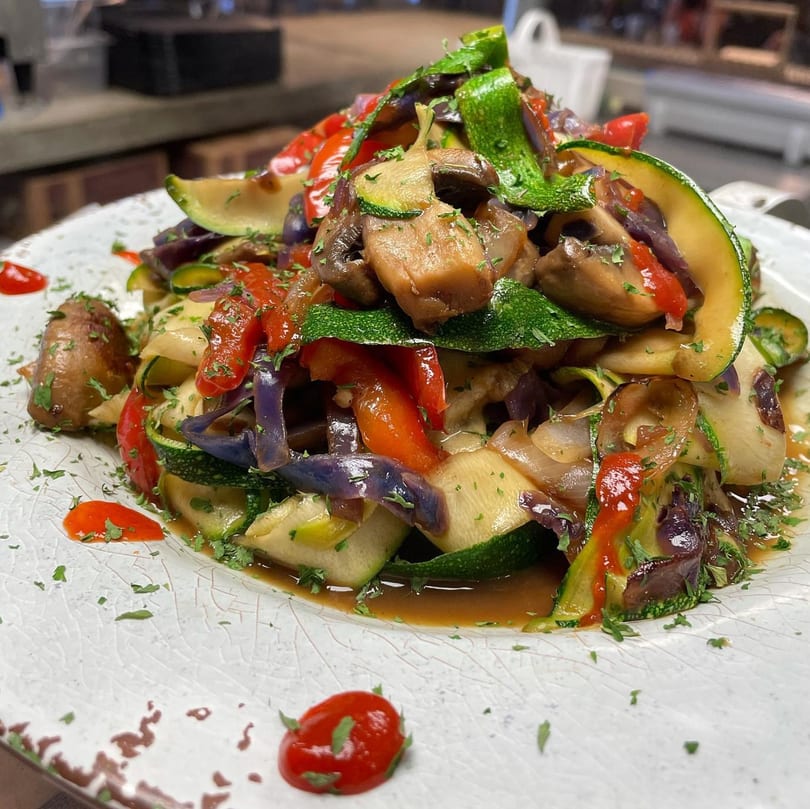 A vibrant medley of sautéed zucchini, mushrooms, red peppers, and onions on a white plate.
