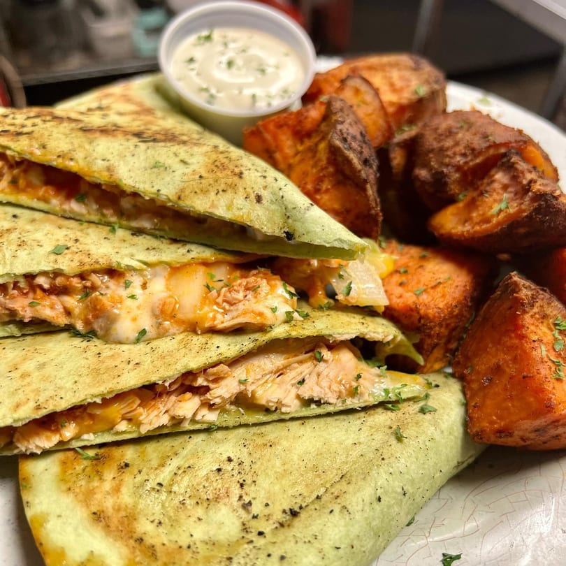 Chicken quesadillas with melted cheese and a side of roasted sweet potatoes and dipping sauce.