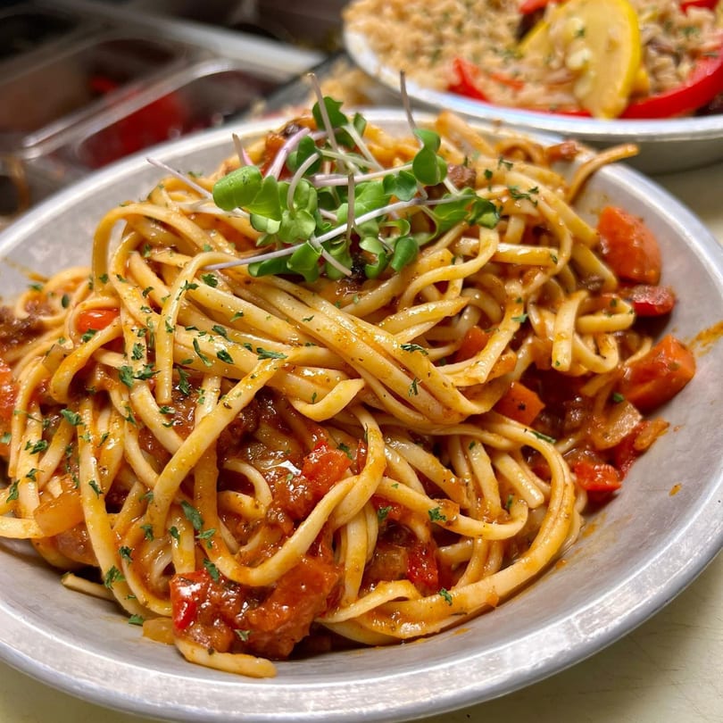 Close-up of Farm Fresh Fast's pasta dish with tomato sauce, herbs, and microgreens in a metal bowl.