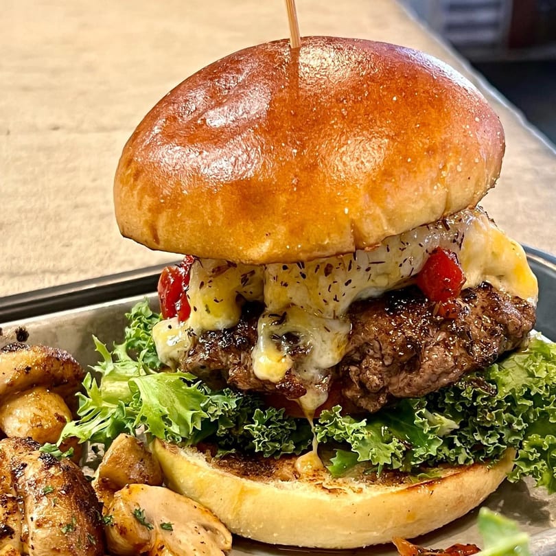 A Farm Fresh Fast burger with melted cheese, red peppers, and lettuce, served with roasted potatoes.